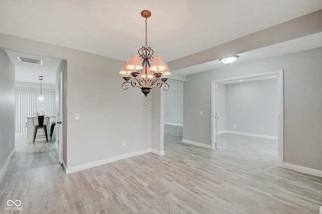 empty room featuring a textured ceiling, a chandelier, and light hardwood / wood-style flooring