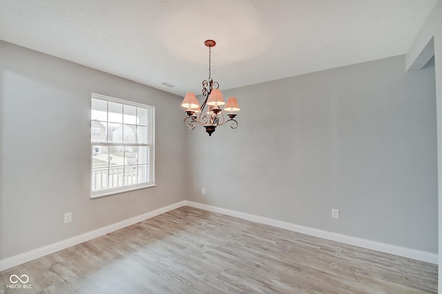 unfurnished room featuring an inviting chandelier, a textured ceiling, and light hardwood / wood-style floors