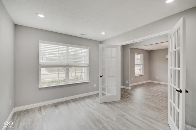 empty room with a textured ceiling, light hardwood / wood-style floors, and french doors