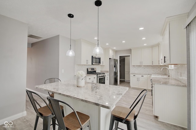 kitchen with sink, white cabinetry, stainless steel appliances, light stone counters, and decorative light fixtures