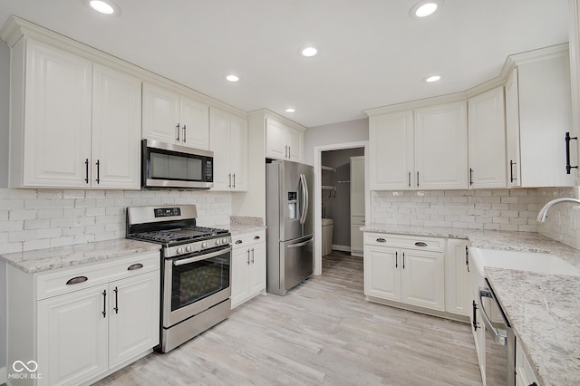 kitchen with white cabinetry, sink, light stone counters, light hardwood / wood-style floors, and stainless steel appliances