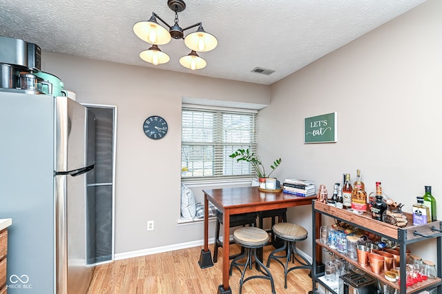 dining area featuring a notable chandelier, light hardwood / wood-style flooring, and a textured ceiling