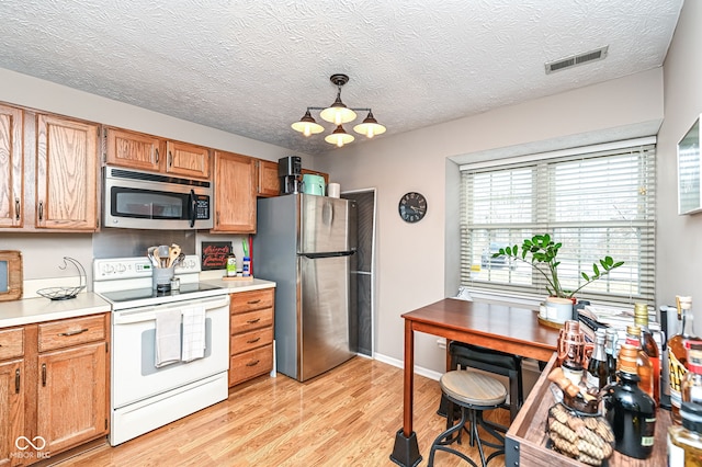 kitchen featuring decorative light fixtures, stainless steel appliances, light hardwood / wood-style floors, and a textured ceiling