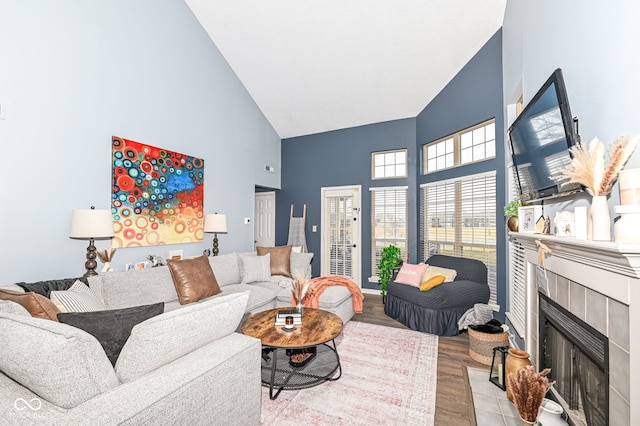 living room with high vaulted ceiling, a tile fireplace, and light hardwood / wood-style floors