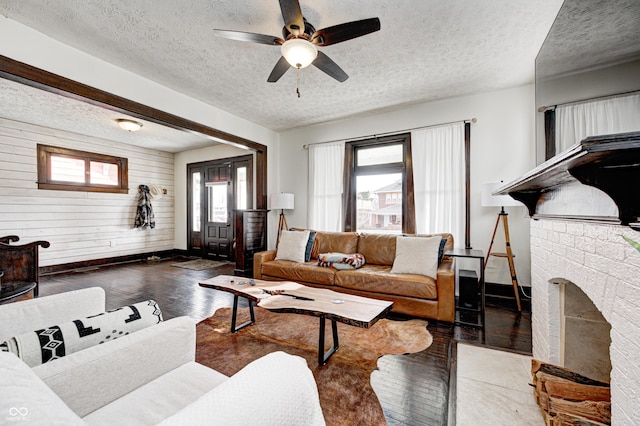 living room featuring a textured ceiling, wooden walls, ceiling fan, a fireplace, and hardwood / wood-style floors