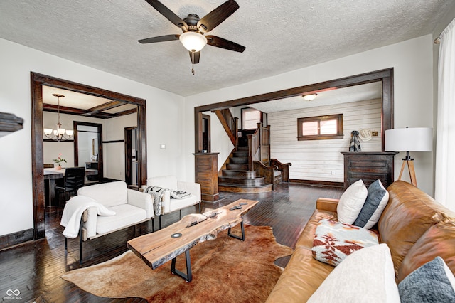 living room with ceiling fan with notable chandelier, dark wood-type flooring, a textured ceiling, and wood walls