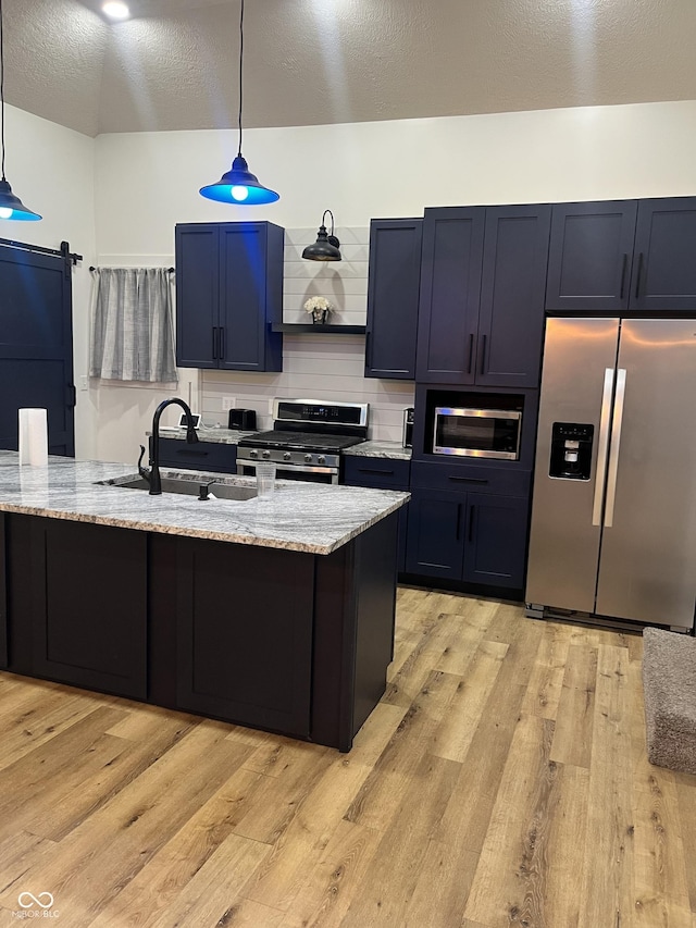 kitchen featuring stainless steel appliances, light stone countertops, a barn door, and decorative light fixtures