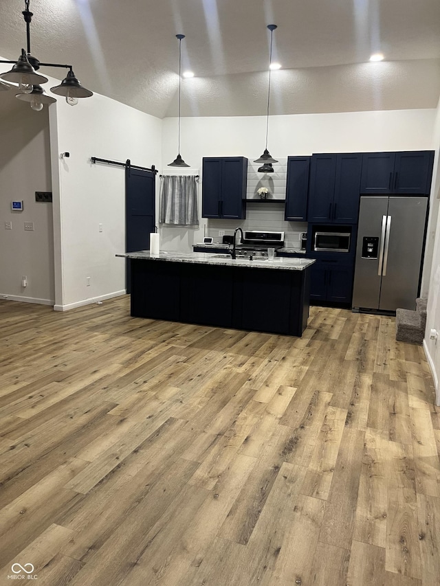 kitchen featuring sink, hanging light fixtures, stainless steel refrigerator with ice dispenser, light stone countertops, and a barn door