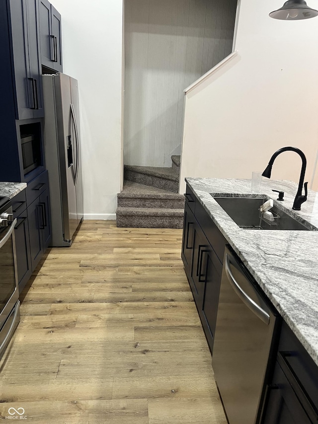 kitchen featuring sink, light stone countertops, light hardwood / wood-style floors, and appliances with stainless steel finishes