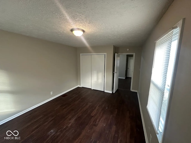 unfurnished bedroom featuring dark hardwood / wood-style floors, a textured ceiling, and a closet