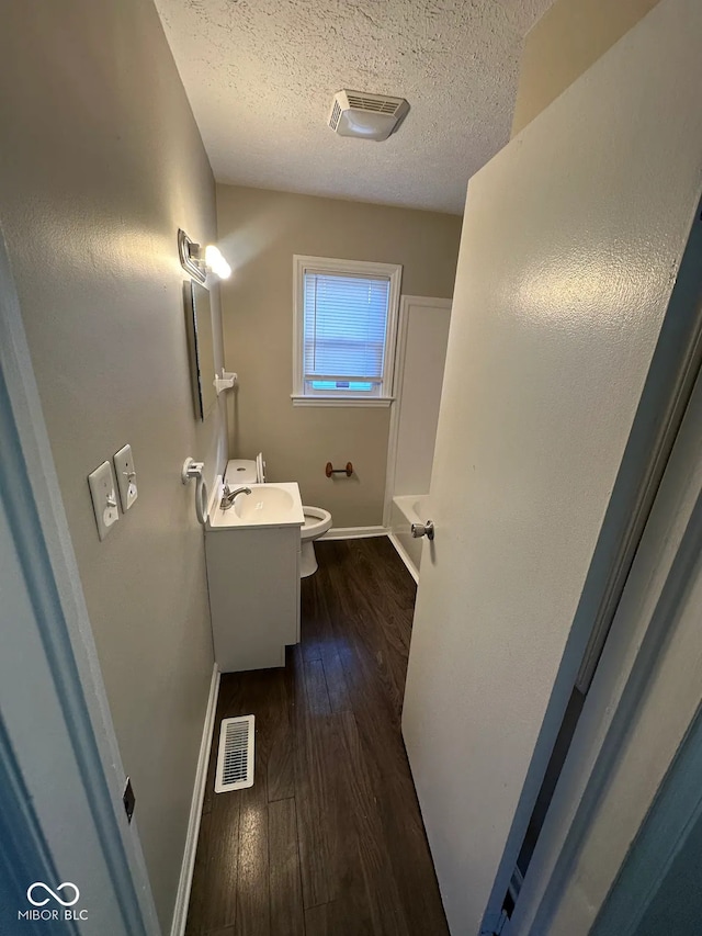 bathroom with hardwood / wood-style floors, vanity, toilet, a bath, and a textured ceiling