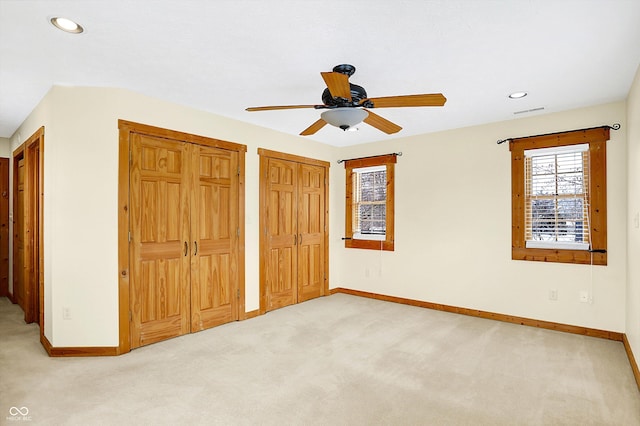 unfurnished bedroom featuring baseboards, light colored carpet, and two closets