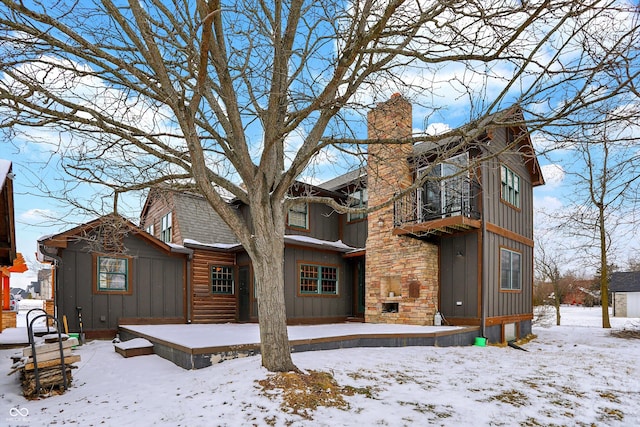 snow covered back of property featuring a fireplace, a chimney, a shingled roof, and board and batten siding