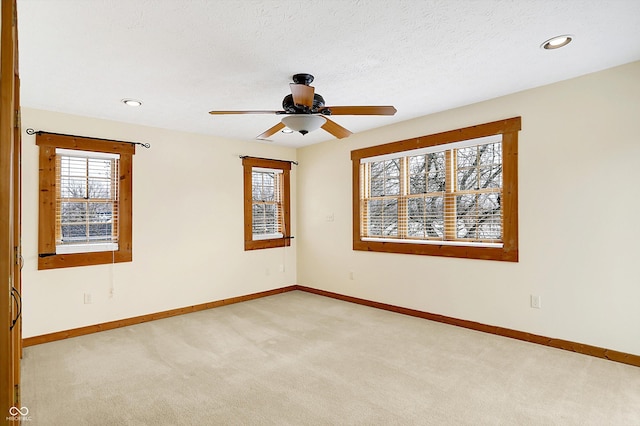 empty room with light colored carpet, ceiling fan, baseboards, and a textured ceiling