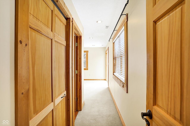 corridor with baseboards, visible vents, and light colored carpet