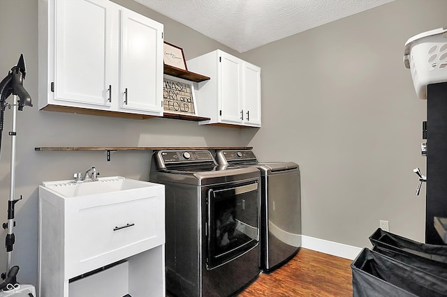 clothes washing area featuring sink, washing machine and dryer, cabinets, wood-type flooring, and a textured ceiling