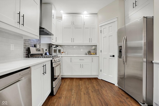 kitchen featuring appliances with stainless steel finishes, dark hardwood / wood-style floors, white cabinets, decorative backsplash, and wall chimney exhaust hood