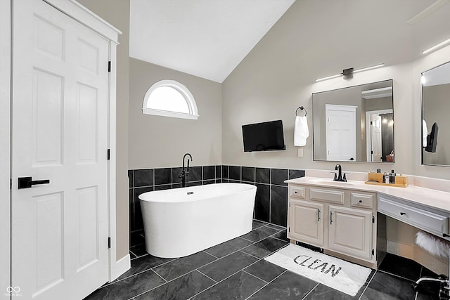 bathroom featuring lofted ceiling, tile walls, a bathtub, vanity, and tile patterned floors