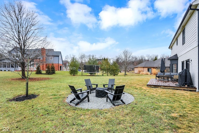 view of yard featuring a trampoline, a wooden deck, and an outdoor fire pit