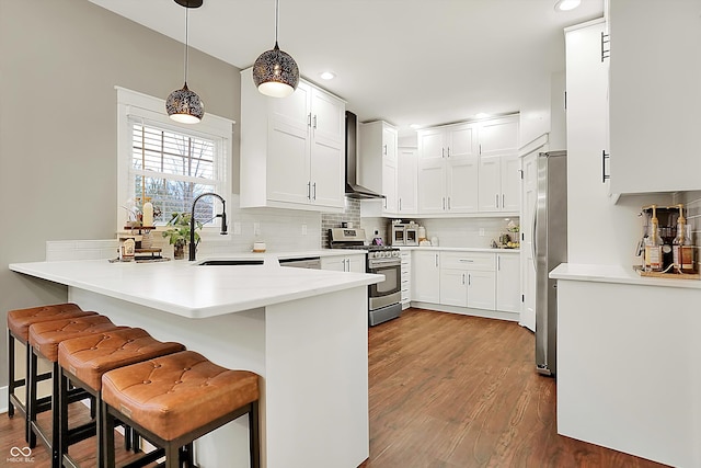 kitchen featuring decorative light fixtures, appliances with stainless steel finishes, a kitchen breakfast bar, wall chimney range hood, and white cabinets