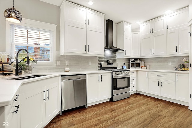 kitchen with appliances with stainless steel finishes, pendant lighting, sink, white cabinets, and wall chimney exhaust hood