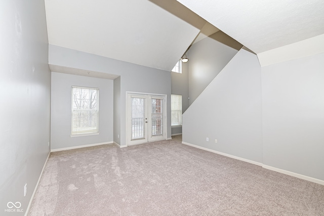 unfurnished living room with french doors, high vaulted ceiling, and light carpet