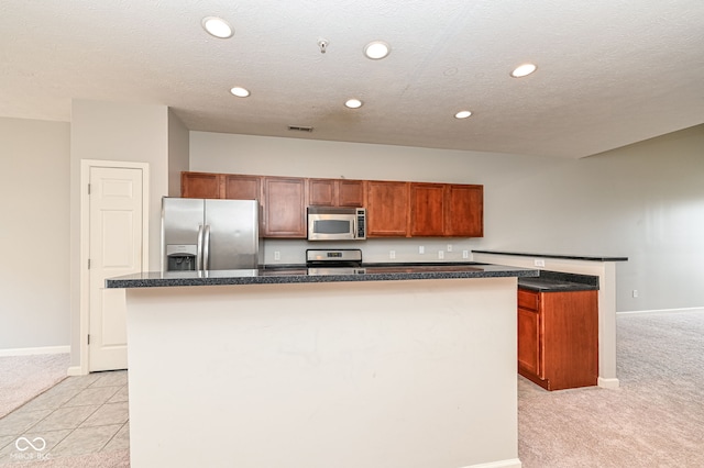 kitchen with appliances with stainless steel finishes, light carpet, a center island with sink, and a textured ceiling