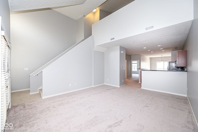 unfurnished living room with light colored carpet and a towering ceiling