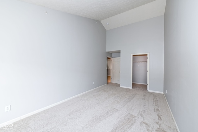 unfurnished bedroom with high vaulted ceiling, a spacious closet, light colored carpet, a textured ceiling, and a closet