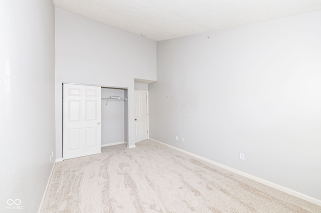 unfurnished bedroom featuring light colored carpet, a closet, a textured ceiling, and a high ceiling