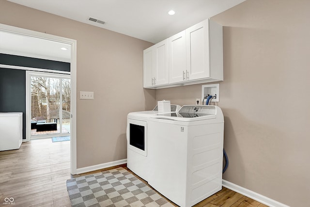 washroom featuring cabinets, washing machine and dryer, and light hardwood / wood-style flooring