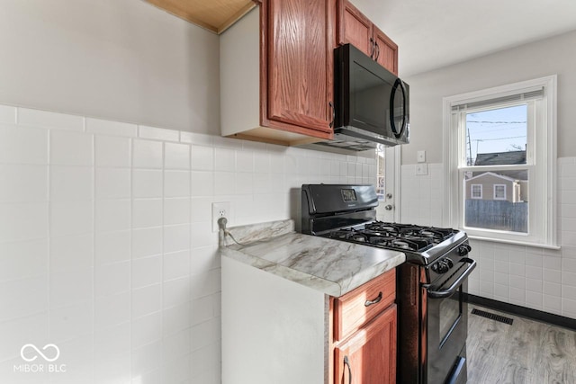 kitchen with tile walls, light wood-type flooring, and black appliances