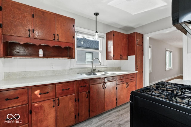 kitchen featuring black gas stove, sink, hanging light fixtures, and light wood-type flooring