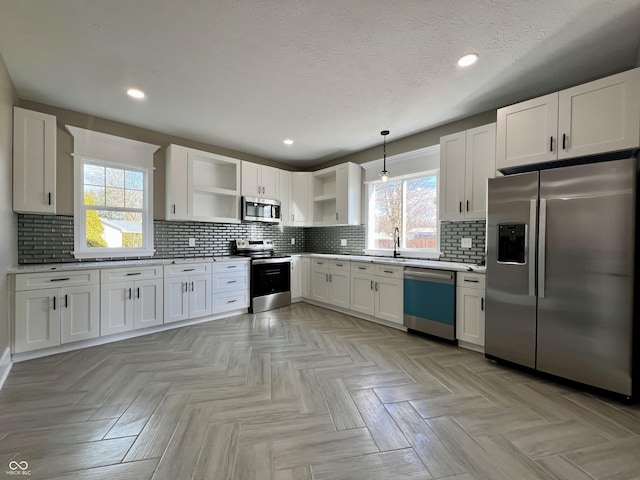 kitchen with stainless steel appliances, white cabinetry, hanging light fixtures, and decorative backsplash