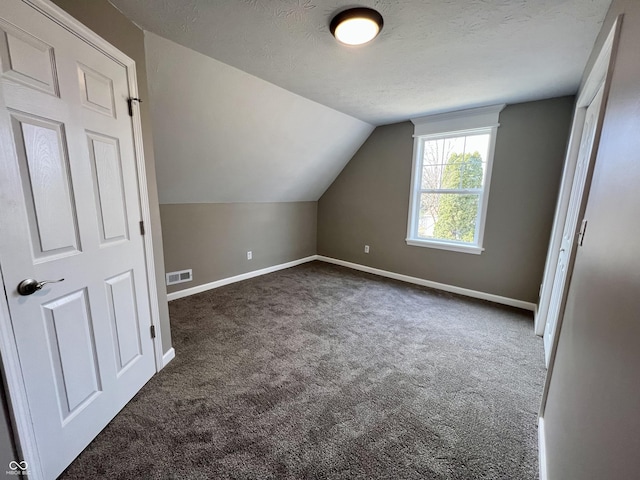 additional living space with vaulted ceiling, a textured ceiling, and dark colored carpet