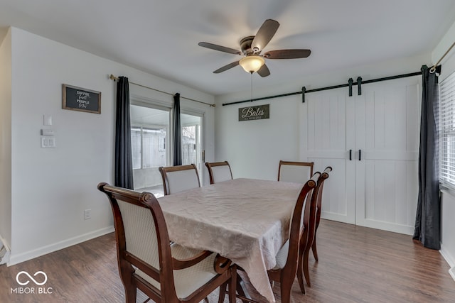 dining area featuring a barn door, dark wood-type flooring, and ceiling fan