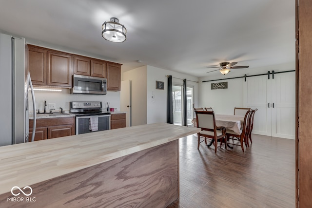 kitchen with stainless steel appliances, a barn door, dark hardwood / wood-style floors, and ceiling fan