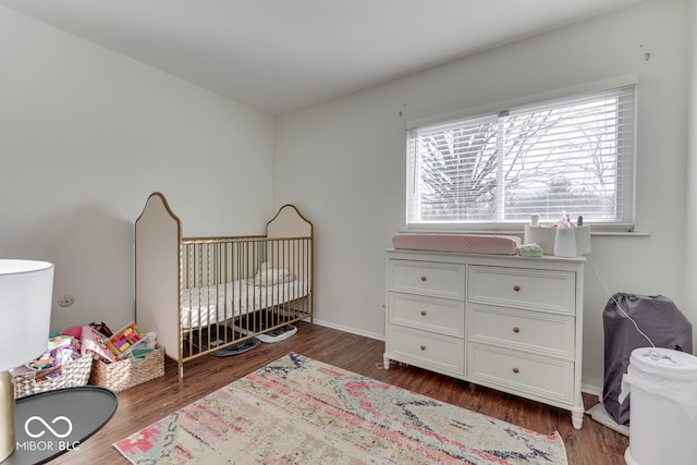 bedroom with dark wood-type flooring and a crib