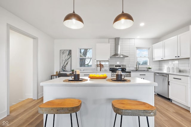 kitchen with pendant lighting, white cabinetry, wall chimney exhaust hood, and stainless steel appliances