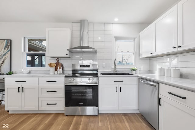 kitchen featuring wall chimney exhaust hood, appliances with stainless steel finishes, sink, and white cabinets