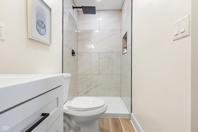 bathroom featuring hardwood / wood-style flooring, vanity, a tile shower, and toilet