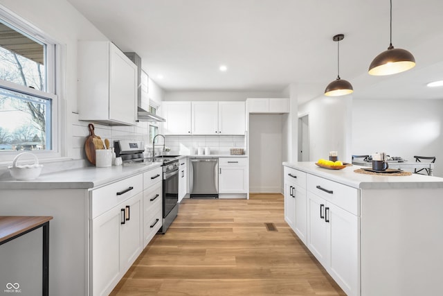 kitchen with decorative light fixtures, stainless steel appliances, decorative backsplash, and white cabinets