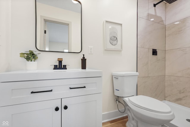 bathroom featuring hardwood / wood-style flooring, tiled shower, vanity, and toilet