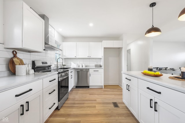 kitchen featuring sink, white cabinets, hanging light fixtures, stainless steel appliances, and light wood-type flooring