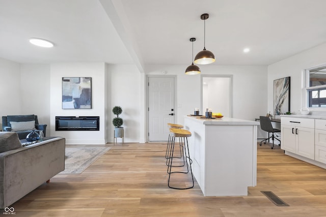 kitchen with a breakfast bar, built in desk, pendant lighting, white cabinetry, and light hardwood / wood-style flooring