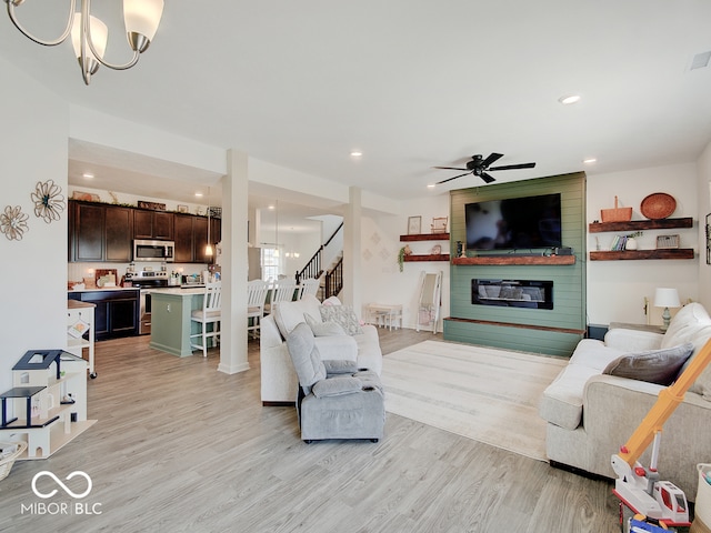 living room featuring a large fireplace, ceiling fan with notable chandelier, and light hardwood / wood-style flooring