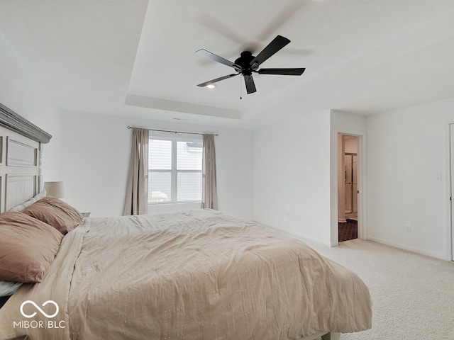 bedroom with ceiling fan, light colored carpet, a raised ceiling, and ensuite bath