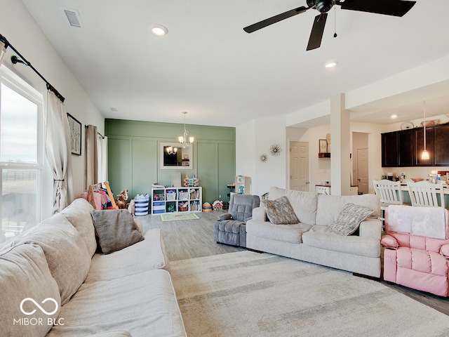 living room featuring ceiling fan with notable chandelier and light hardwood / wood-style flooring