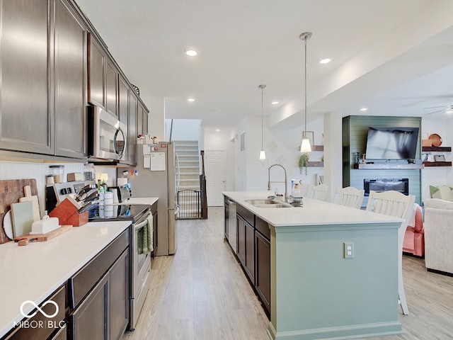 kitchen with sink, a center island with sink, appliances with stainless steel finishes, pendant lighting, and light hardwood / wood-style floors