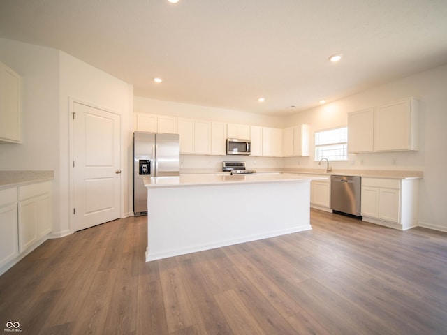 kitchen with appliances with stainless steel finishes, white cabinets, a sink, and wood finished floors